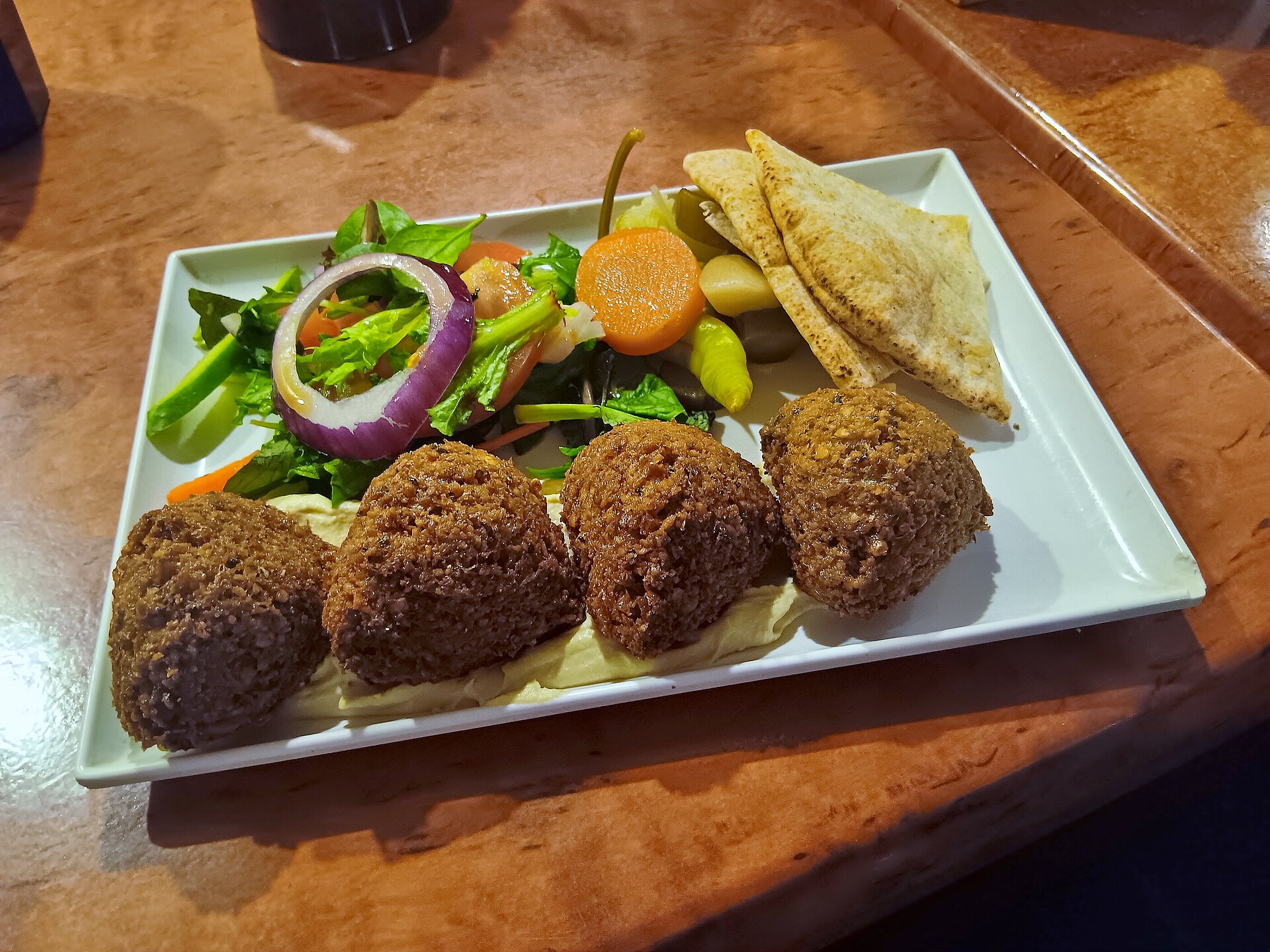 A plate of four falafel at a restaurant, with salad and sauce